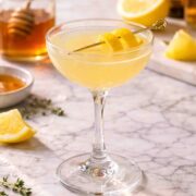 Bee's Knees cocktail in a coupe glass with a jar of honey behind it.