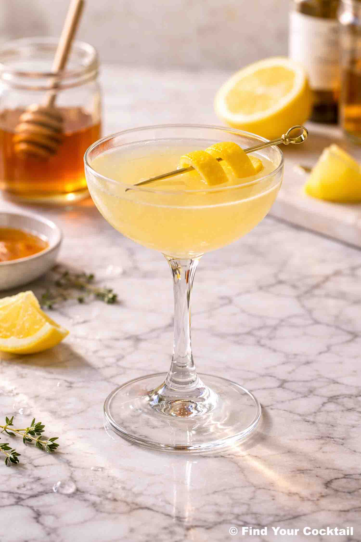 Bee's Knees cocktail in a coupe glass with a jar of honey behind it. 