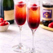 two champagne glasses with kir royale and a bottle of bubbles behind