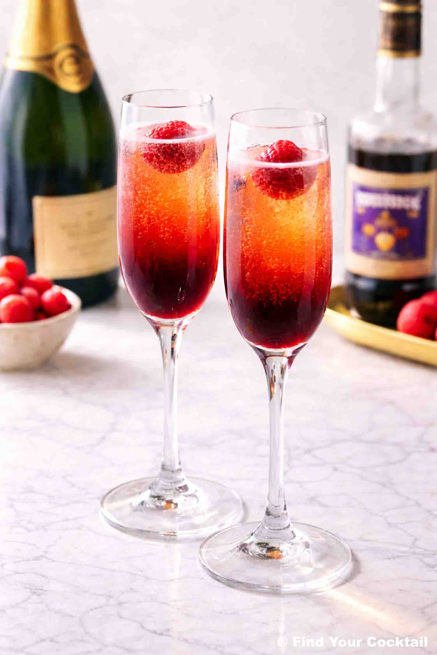 two champagne glasses with kir royale and a bottle of bubbles behind