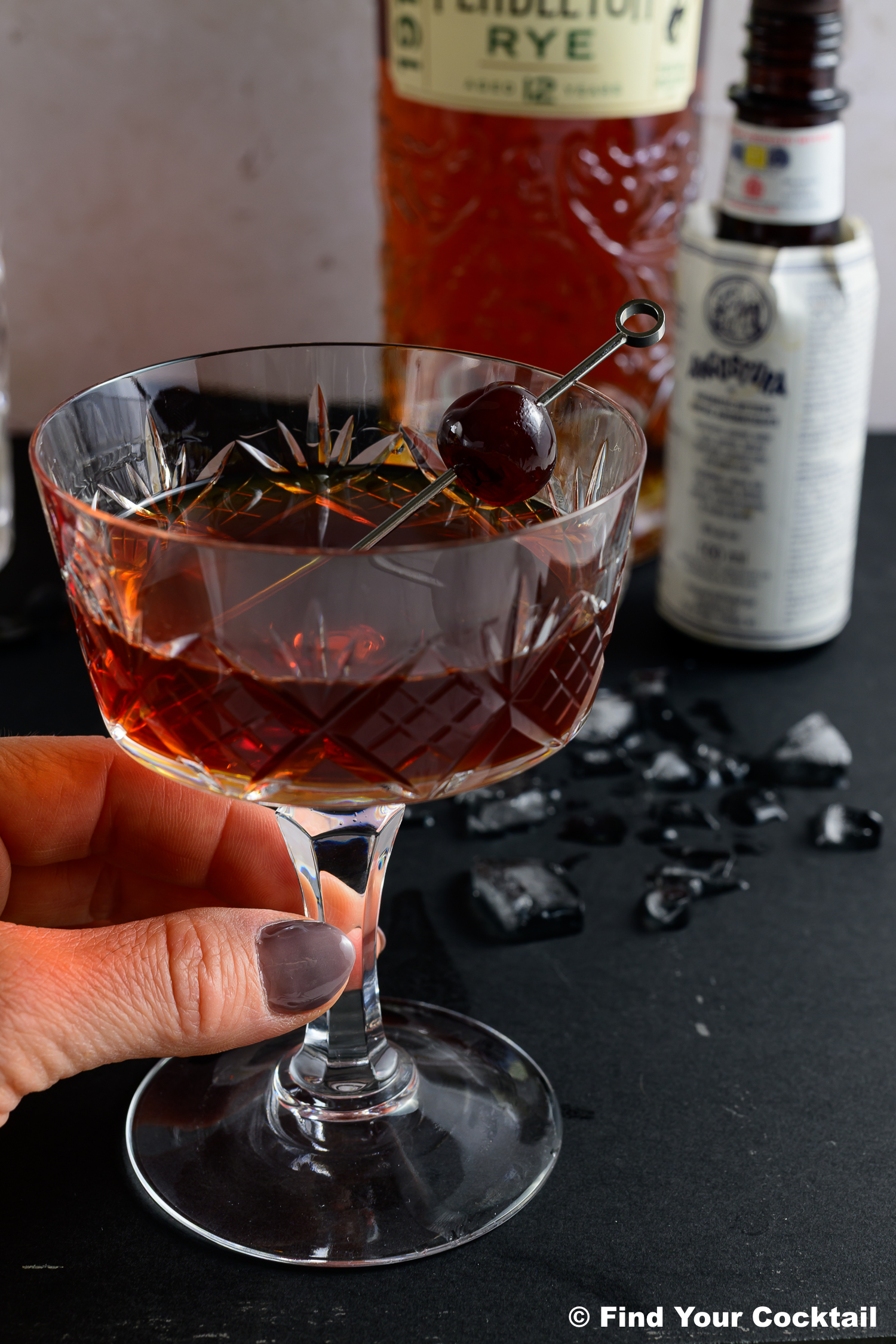 a hand holding a classic manhattan cocktail