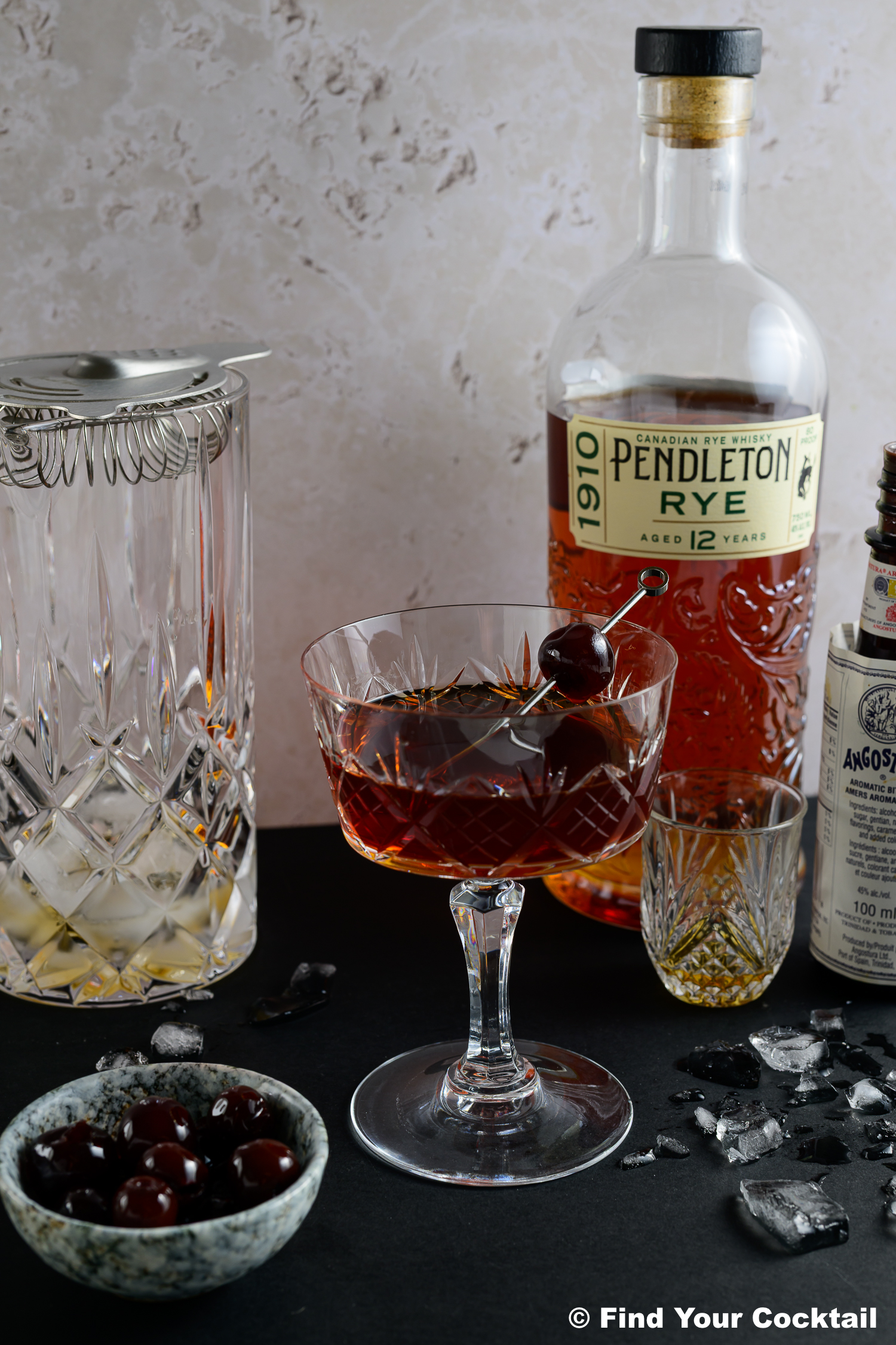a manhattan cocktail in a coupe glass with a cocktail mixer beside.