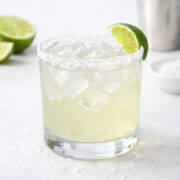 a margarita in a rocks glass rimmed with salt with a lime wedge on the side.