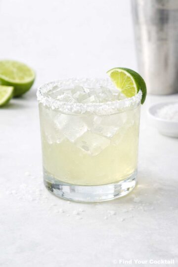 a margarita in a rocks glass rimmed with salt with a lime wedge on the side.