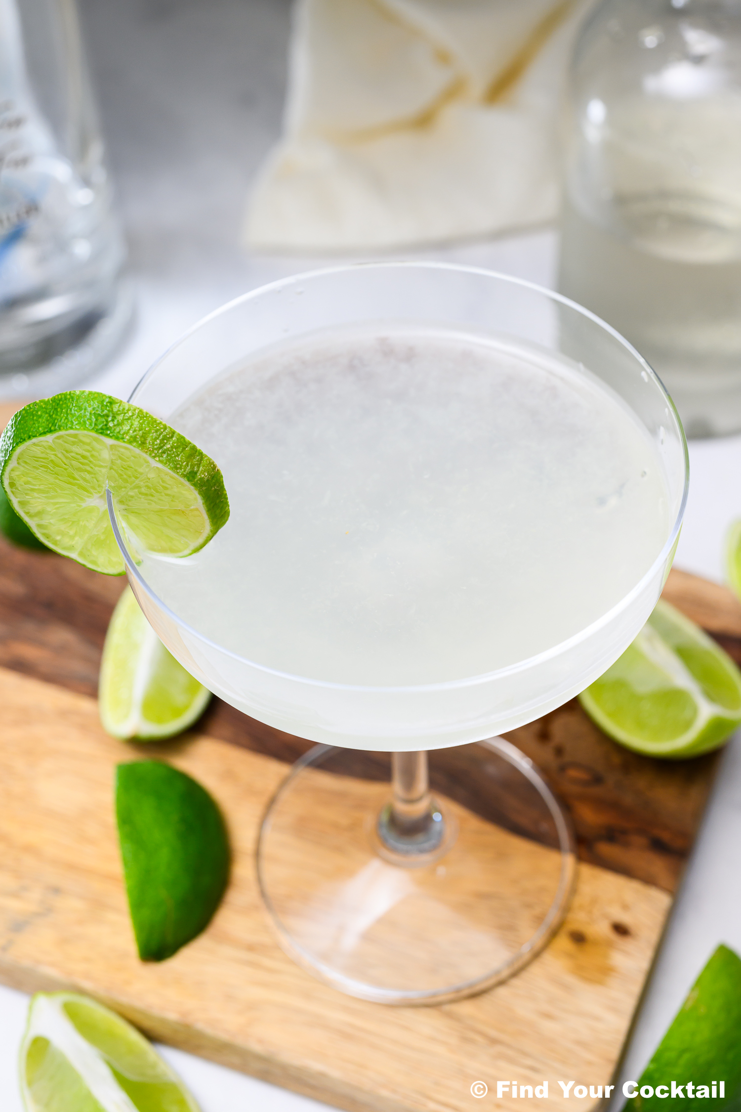 A classic cocktail in a coupe glass garnished with a lime wheel, placed on a wooden board with lime wedges nearby.
