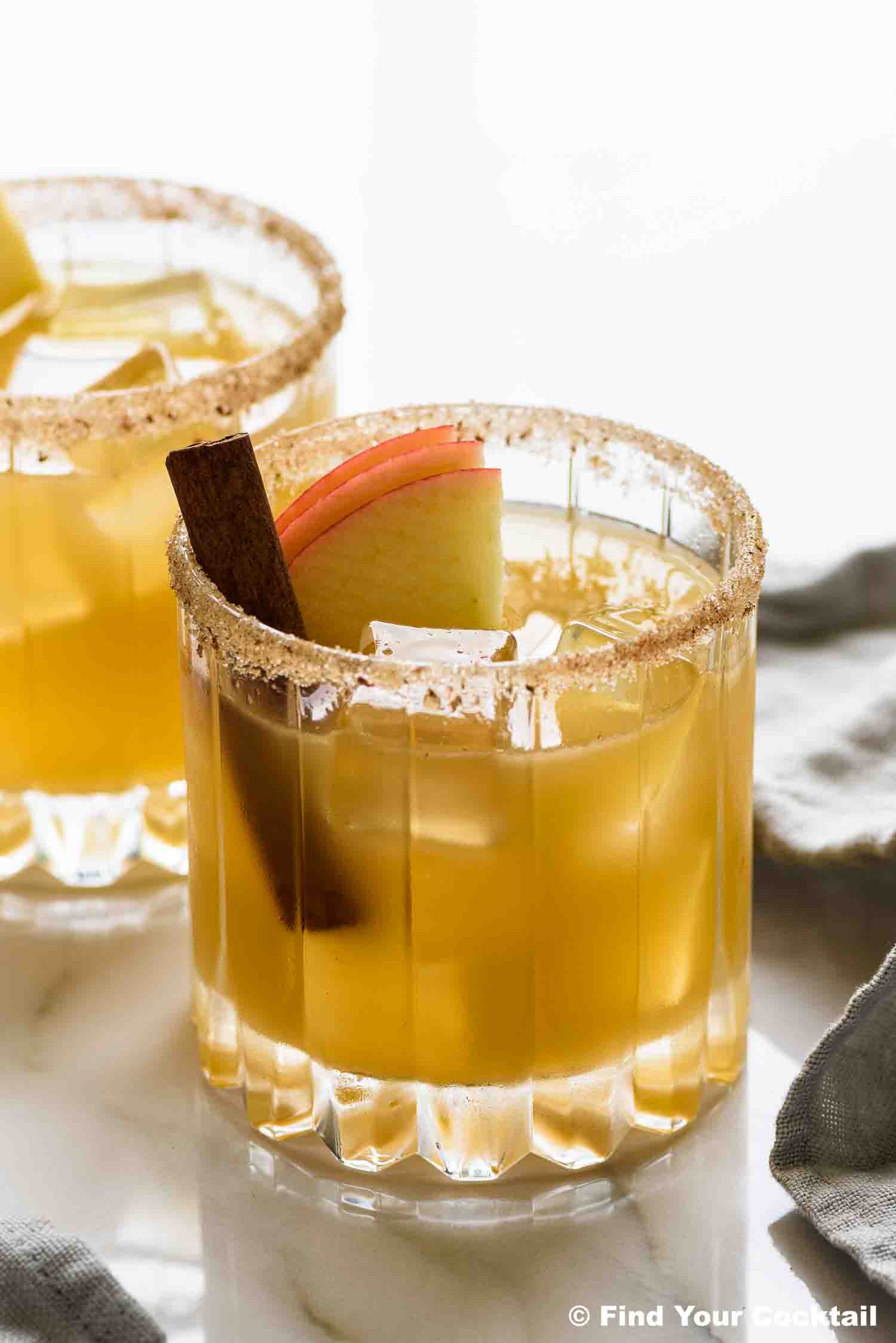 2 cocktails garnished with a cinnamon stick and slices of apples.