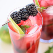 a tall glass of blackberry mojito with limes and blackberries