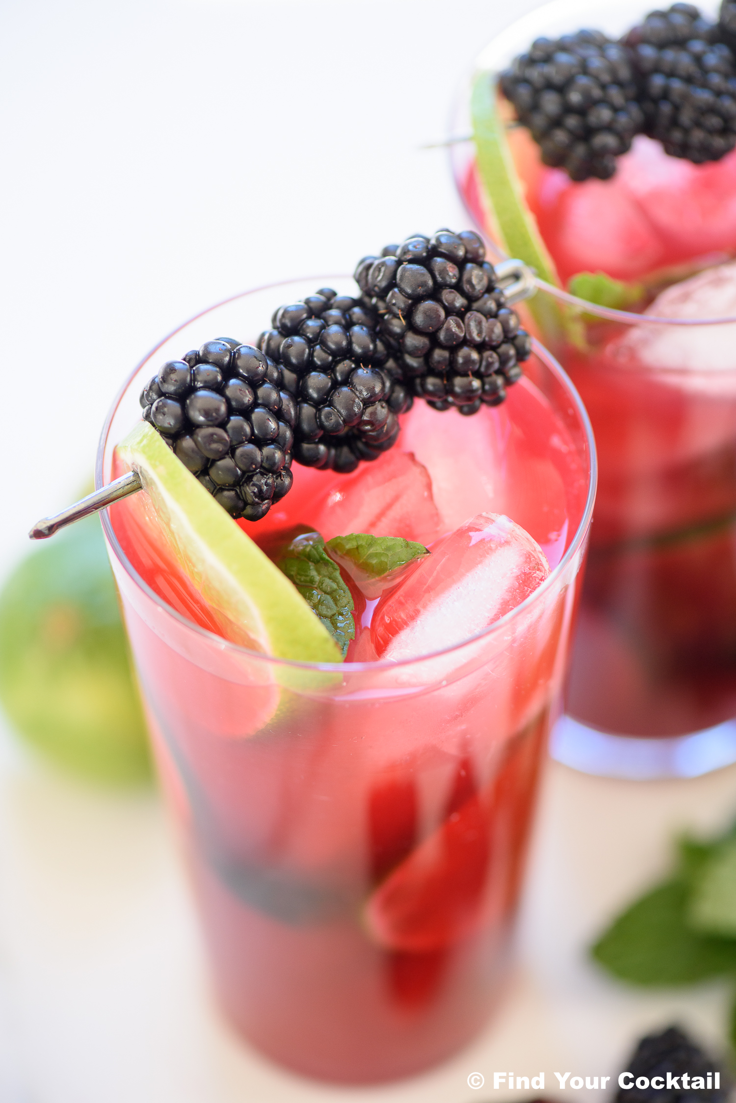 a tall glass of blackberry mojito with limes and blackberries