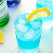 a blue long island iced tea with a lemon slice next to a bottle of blue Cura&ccedil;ao