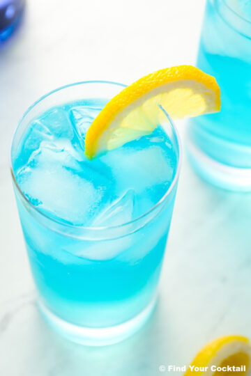 a close up of a blue drink in a tall glass with a lemon slice