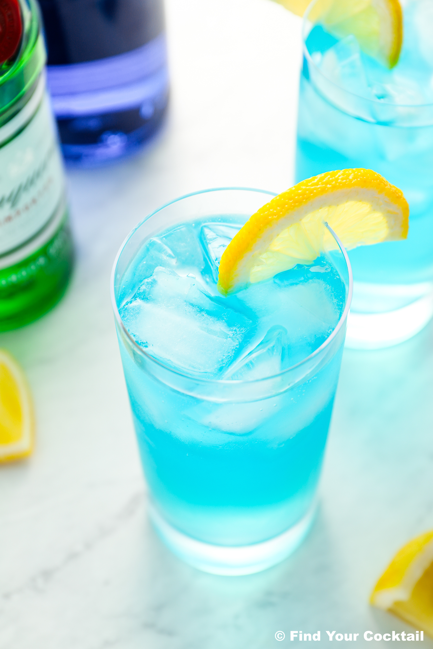 a blue long island iced tea with a lemon slice next to a bottle of blue Curaçao