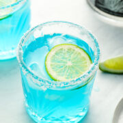 two blue margaritas with limes