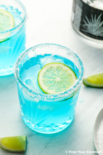 two blue margaritas with limes