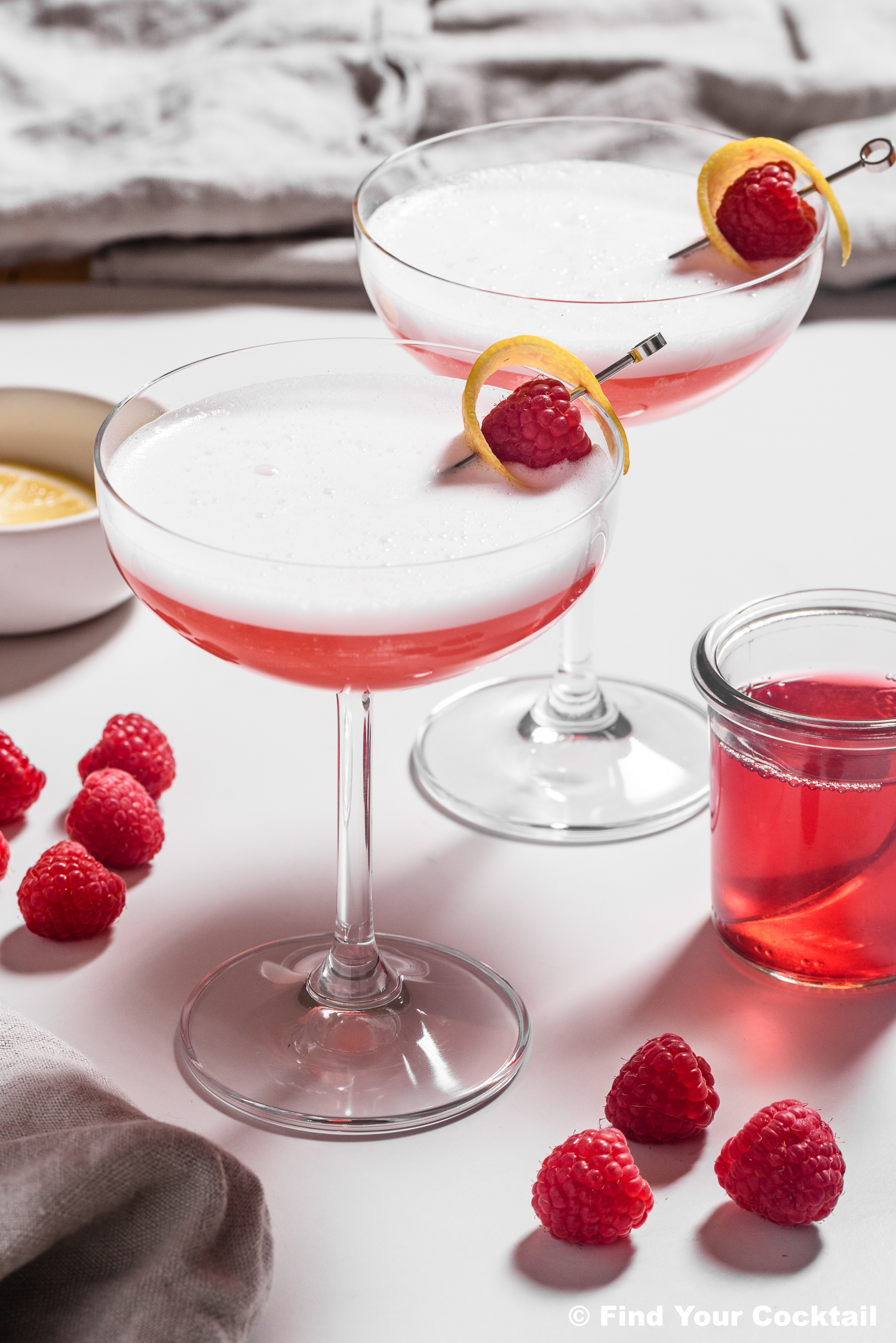 pink cocktails in coupe glasses surrounded by raspberries