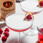two clover club cocktails next to a bottle of vodka
