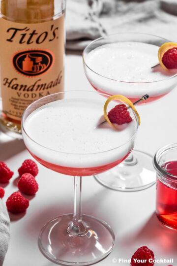 two clover club cocktails next to a bottle of vodka