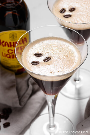 a frothy espresso martini in a martini glass garnished with 3 coffee beans
