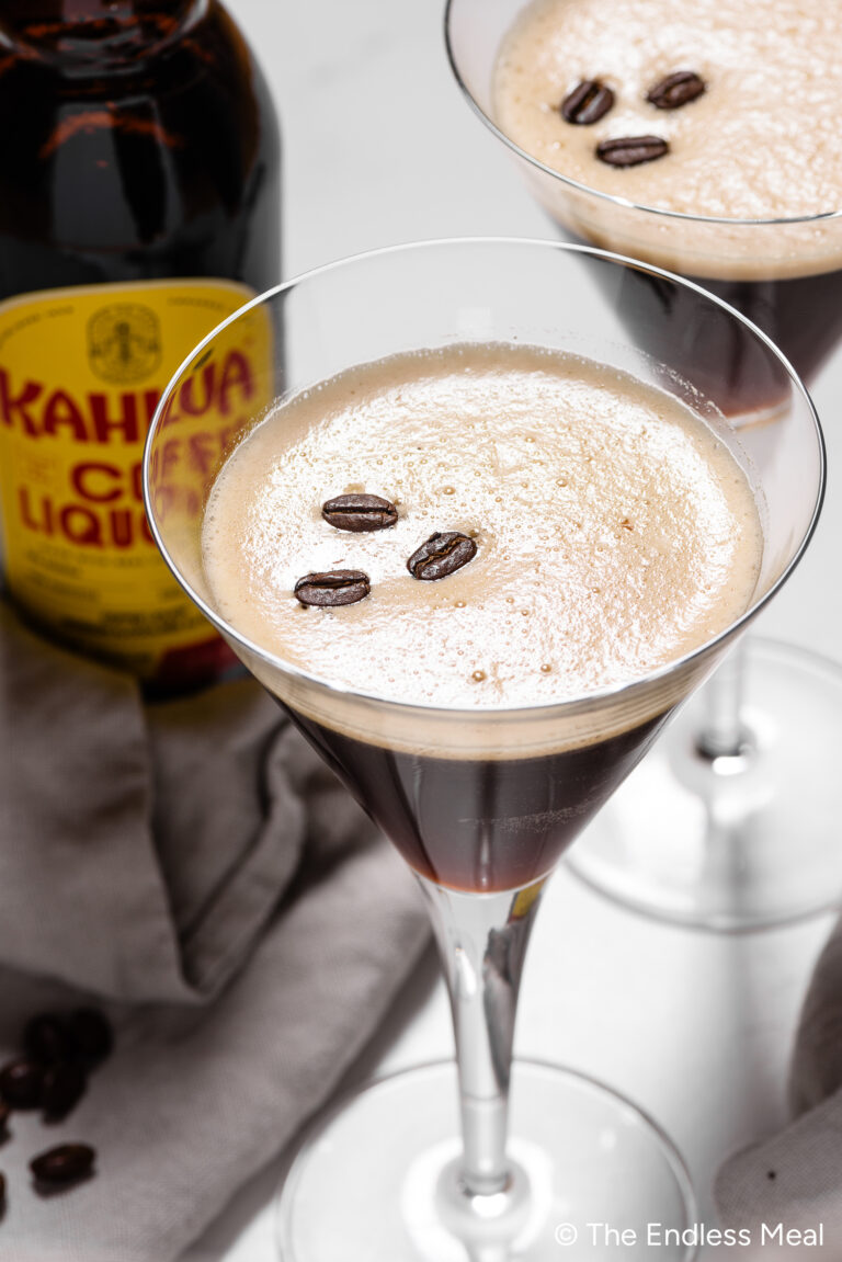 a frothy espresso martini in a martini glass garnished with 3 coffee beans