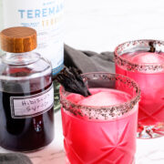 two hibiscus margaritas next to a bottle of hibiscus syrup and a bottle of tequila