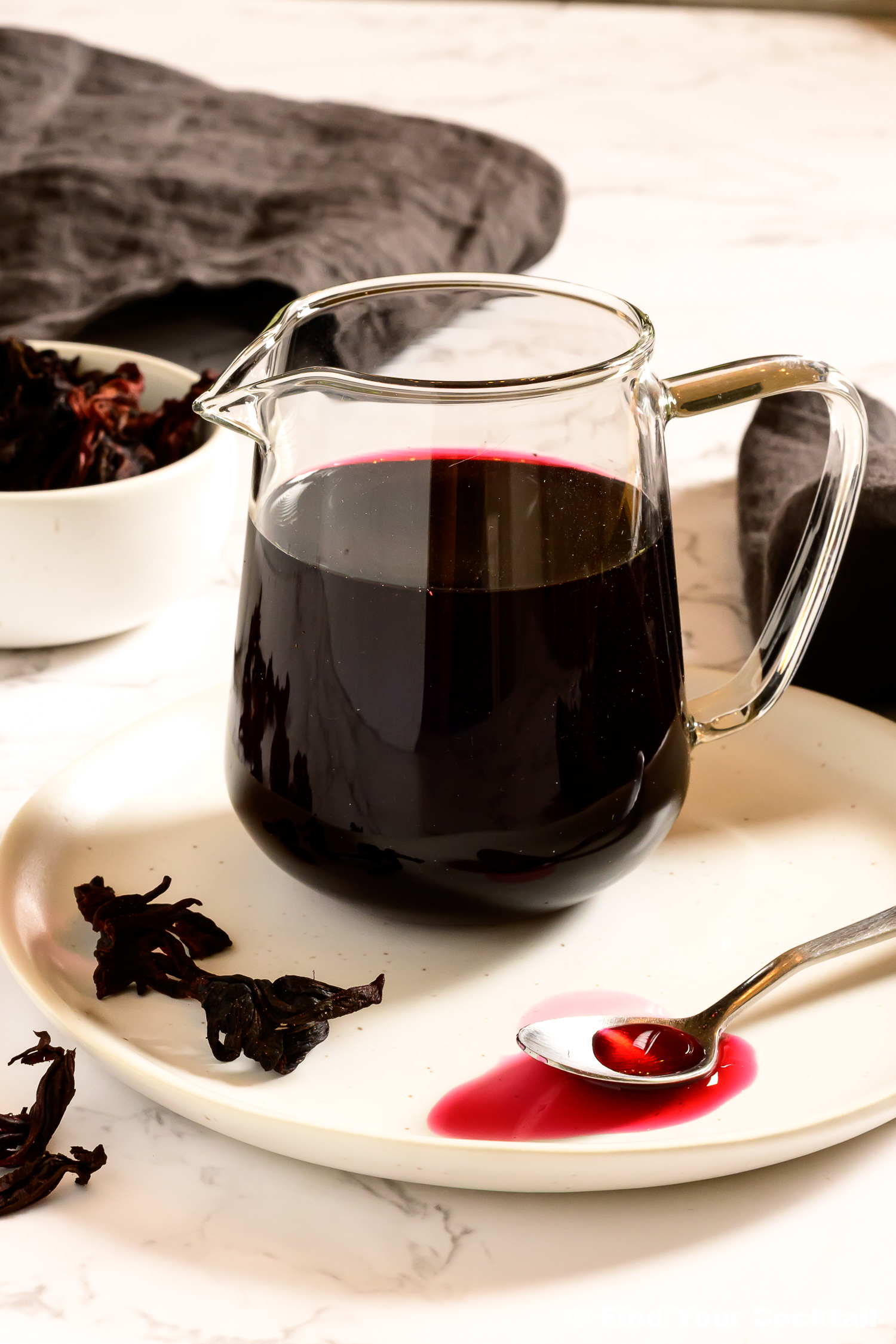 hibiscus syrup in a small glass pitcher with bight pink syrup on a spoon