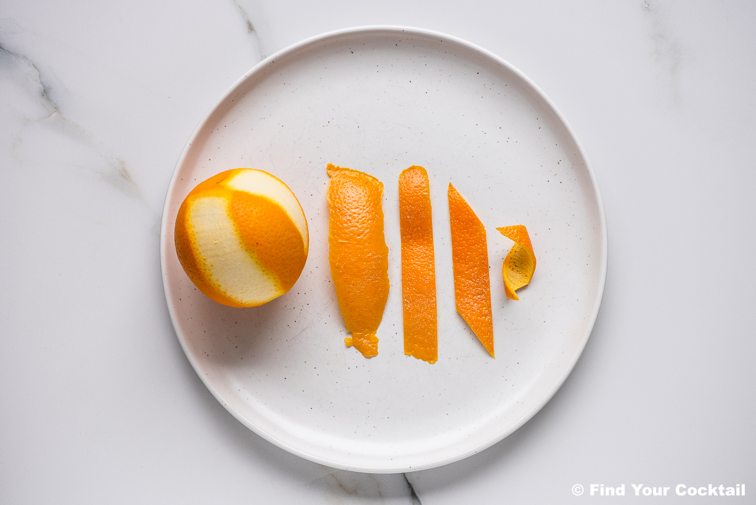 A white plate displays a whole orange with partial peel removed and four orange peel strips arranged by size, from largest to smallest, on a white surface.