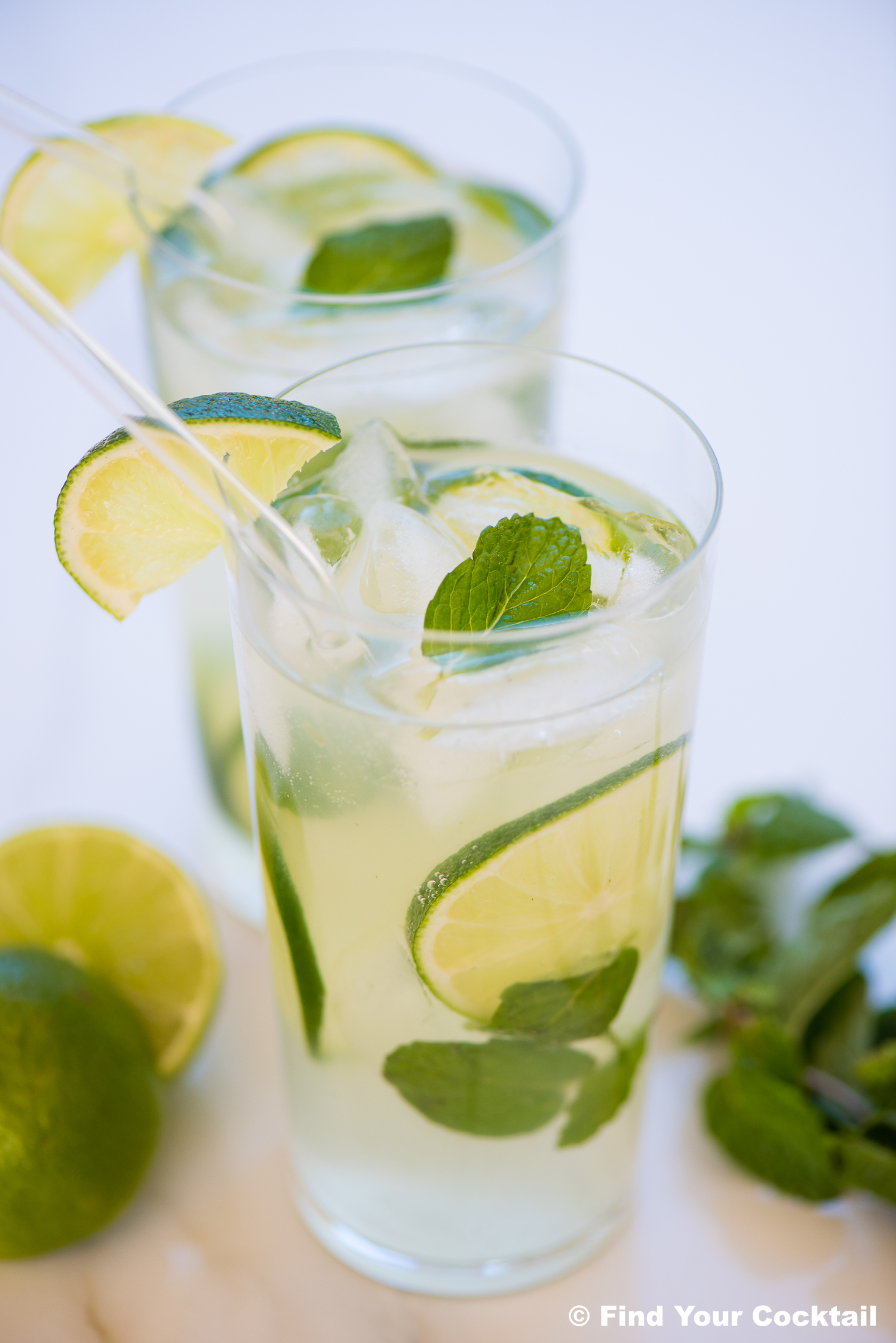2 mojitos in glasses with straws, mint, and limes.