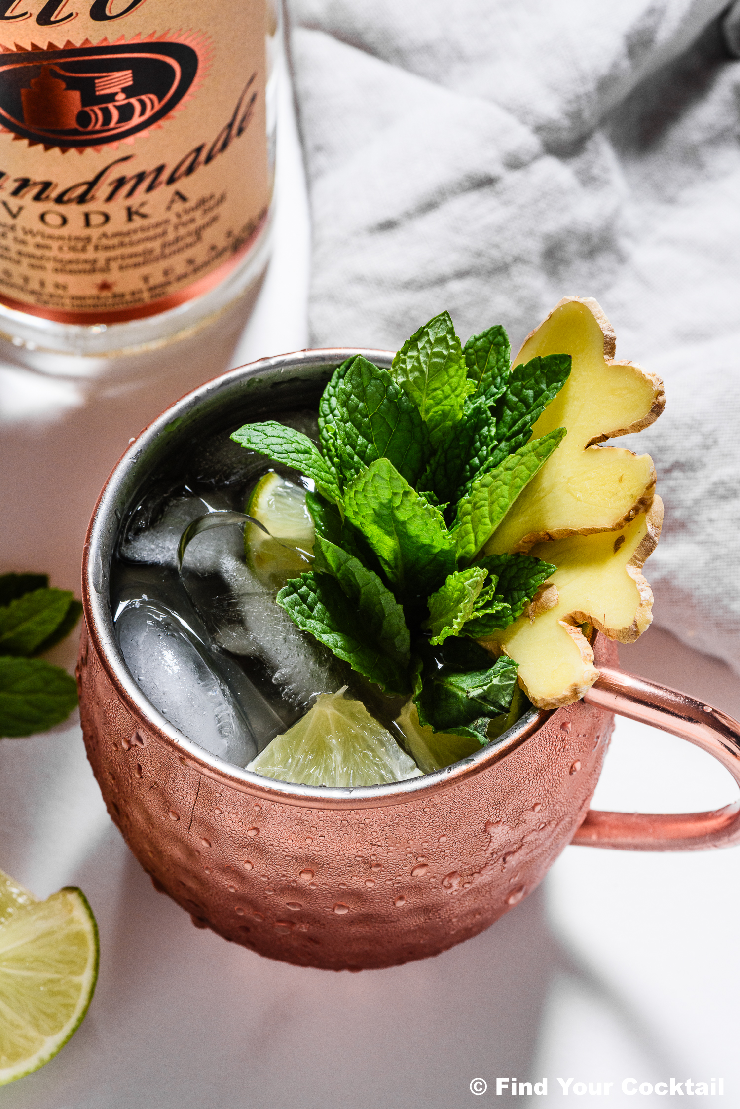 a moscow mule with lots of sliced ginger, mint leaves and some lime wedges in a copper mug with ice.