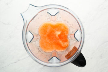 Top-down view of an orange liquid mixture inside a blender on a white surface.