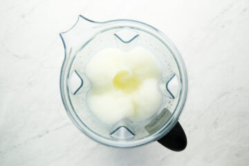 A top-down view of a blender containing a white, icy mixture with a smooth texture, placed on a light-colored surface.