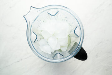 Top-down view of several ice cubes in a clear blender pitcher on a white surface.