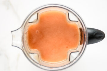 A blender filled with light orange liquid viewed from above, sitting on a white surface.