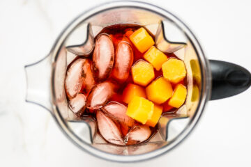 Overhead view of a blender containing ice cubes, Campari, and several orange ice cubes.