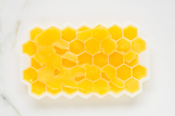 A white silicone ice cube tray with a honeycomb pattern is filled with yellow frozen cubes, some of which have been partially scooped out.