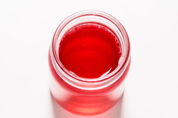 A glass jar filled with red liquid, viewed from above against a white background.