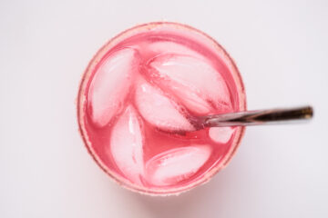 A glass filled with pink liquid, ice cubes, and a metal straw, viewed from above against a plain white background.