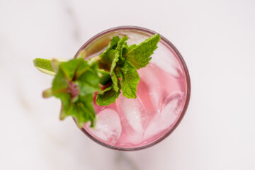 Overhead view of a pink iced drink in a glass, garnished with fresh mint leaves and a lime wedge.