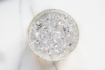 A top-down view of a clear glass filled with small ice cubes, sitting on a white surface.