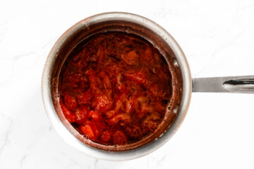 A stainless steel pot filled with simmering tomato sauce, viewed from above, on a white marble surface.