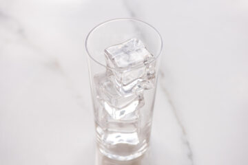 A clear glass filled with several large ice cubes sits on a white marble surface.