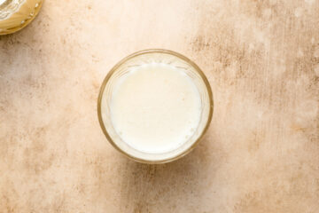 A glass of milk seen from above on a light brown textured surface.