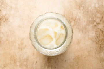 A glass filled with iced milky beverage viewed from above, set on a light, textured surface.