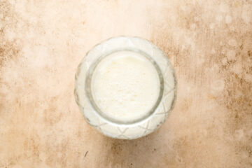 A glass filled with milk photographed from above on a lightly textured beige surface.