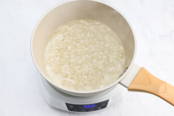 A pot of water is boiling on an electric stovetop with visible bubbles and steam rising from the surface.