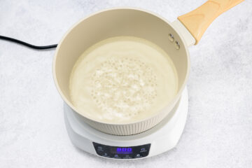 A saucepan with a light-colored liquid boiling on an electric burner with digital controls.