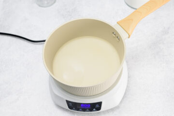 A saucepan with a light-colored liquid is placed on an electric induction cooktop with an illuminated digital display showing 800.