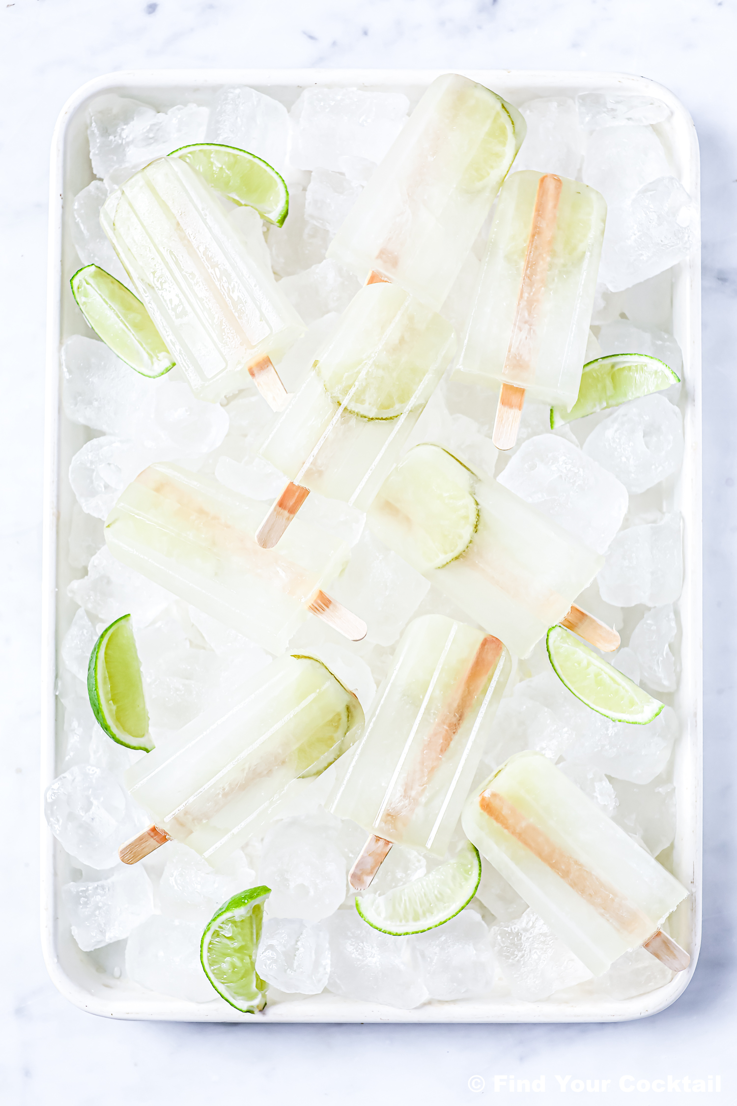 A tray of ice holds several clear popsicles with lime slices inside, garnished with additional lime wedges.