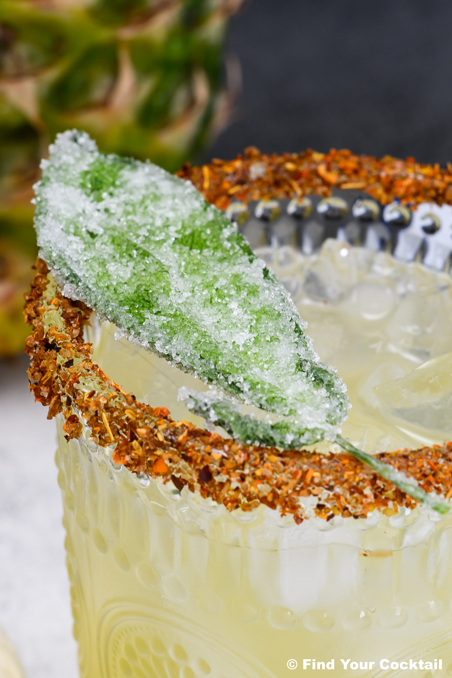 A cocktail in a glass with a spiced rim, ice, and a sugared sage leaf garnish.