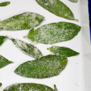 Green leaves coated with sugar crystals are arranged on a white tray.