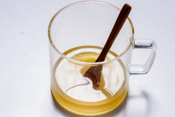A clear glass cup filled with light brown liquid, with a wooden spoon resting inside.