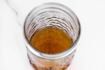 A close-up, top-down view of a glass jar containing a small amount of brown liquid with some sediment visible at the bottom.